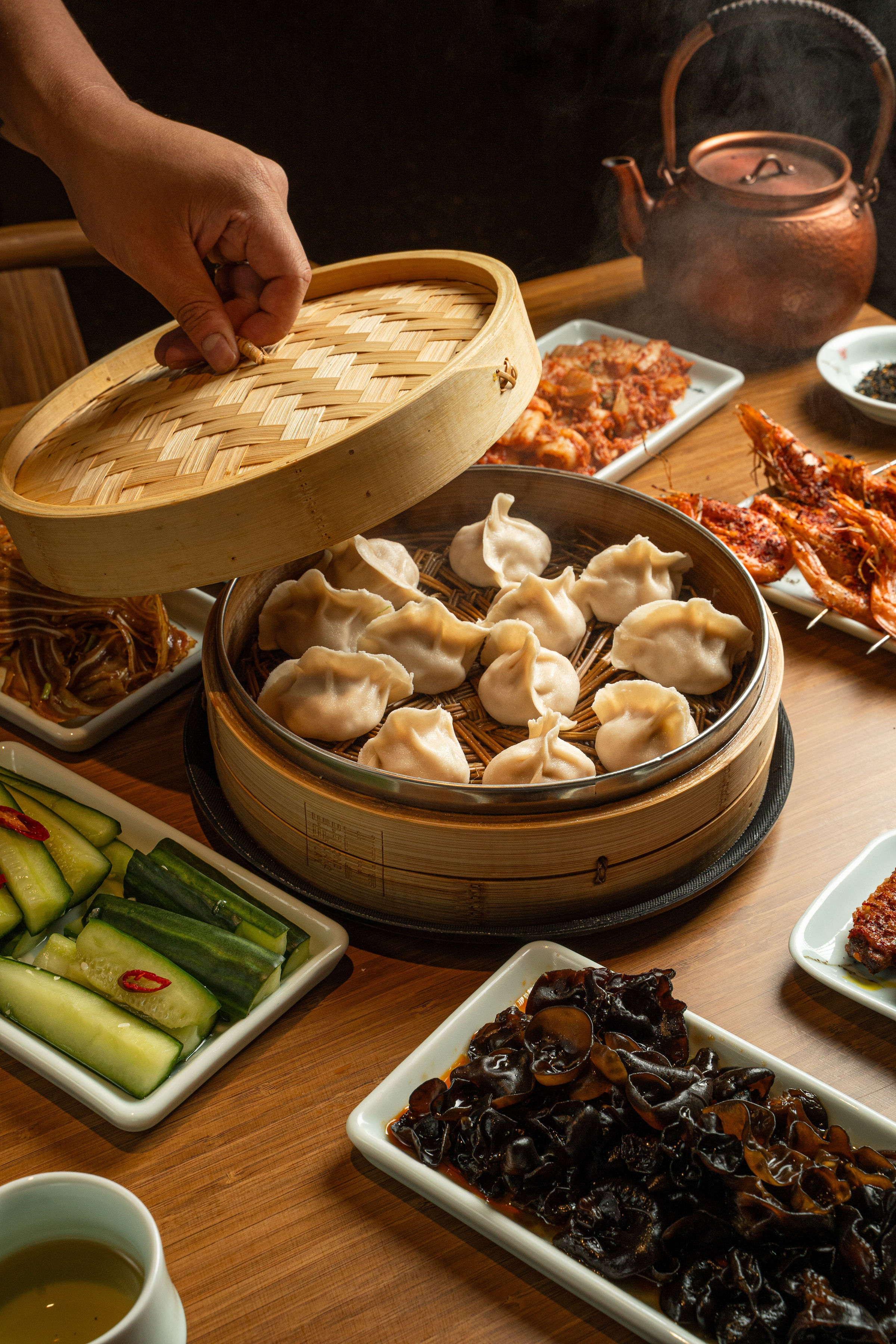Lifting a bamboo steamer lid to reveal freshly prepared dumplings